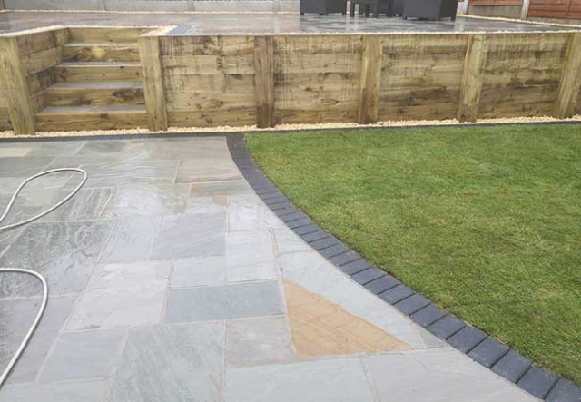 A full rear landscape involving retaining wall using sleepers, patio using a charcoal edging pavior, a kandla grey indian sanstone and grass area returfed at a job in Gedling, Nottingham